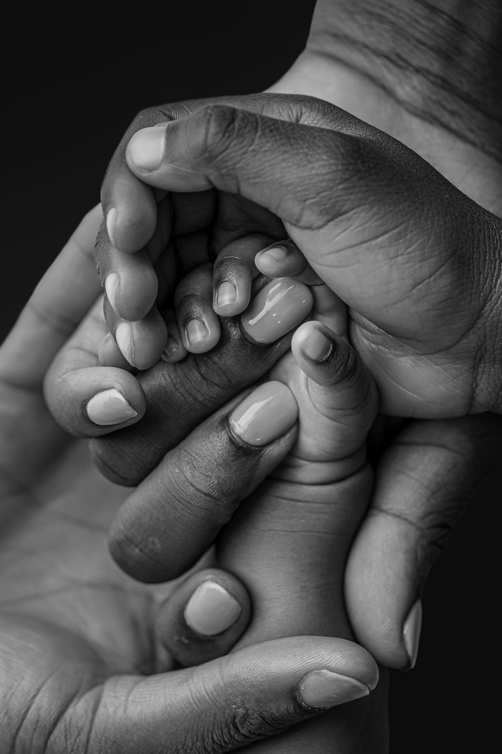 Black and white close-up of adult hands gently cradling a newborn baby's tiny fist, symbolizing love and protection.