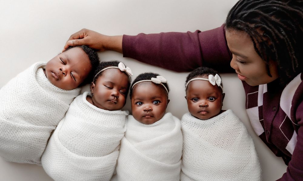 A parent lovingly touches four swaddled newborn babies lying together on a white blanket.