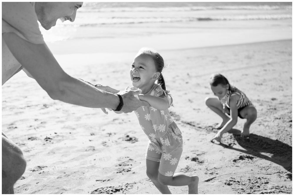 Children laugh and play on the beach with an adult in a fun black and white candid photo in Sayulita.
