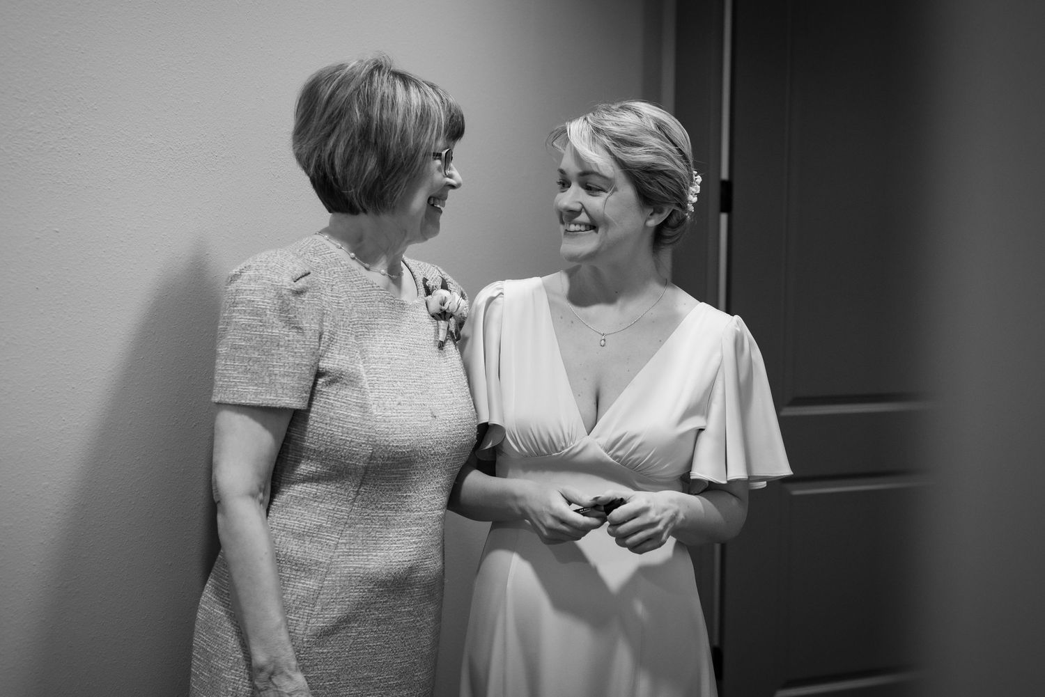 Black and white photo of bride and older woman smiling at each other during wedding preparations.