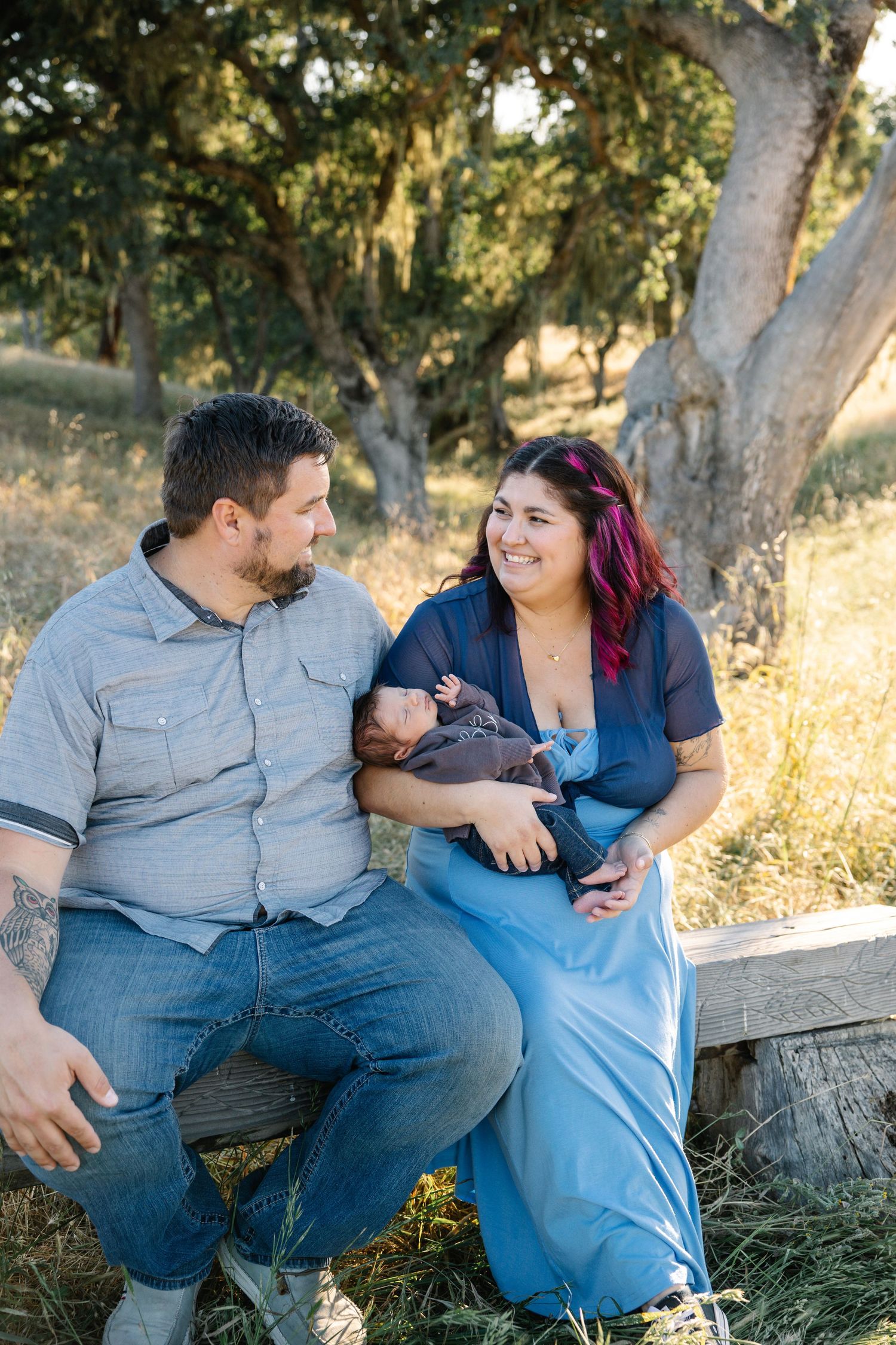 New mom and dad pose with mom holding baby in grass and oak trees during sunset, golden hour photo