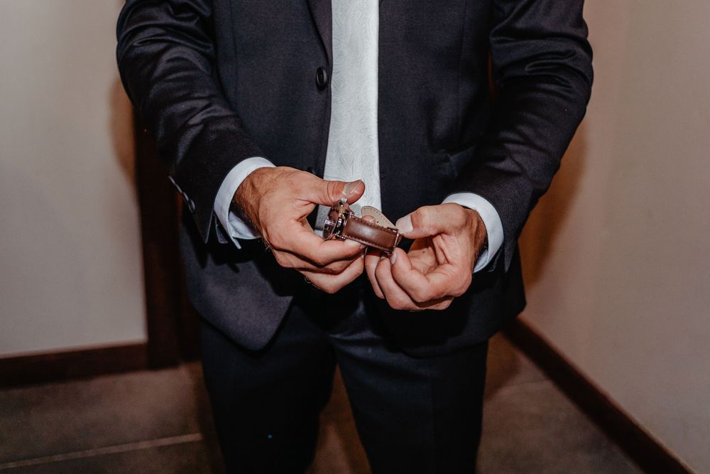 Groom in dark suit holding cufflinks while preparing for wedding ceremony.