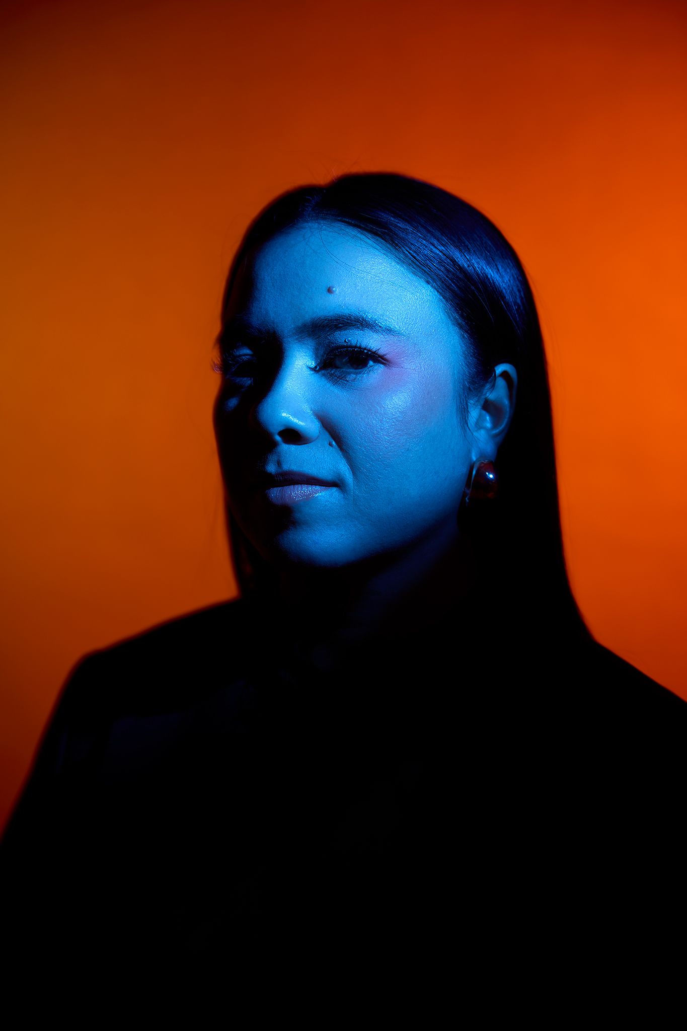 Portrait of a woman with straight dark hair lit by blue and orange neon lights.