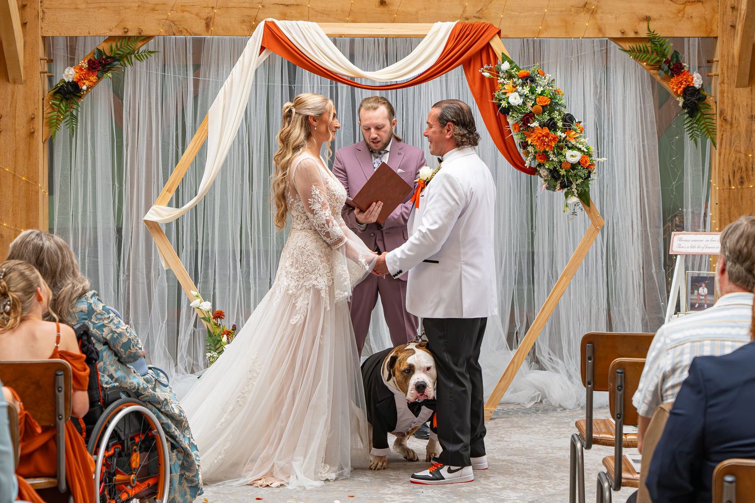 Couple exchanges vows at rustic wedding ceremony under floral arch with officiant and dog.Yorkshire, Sheffield, Lincolnshire, UK