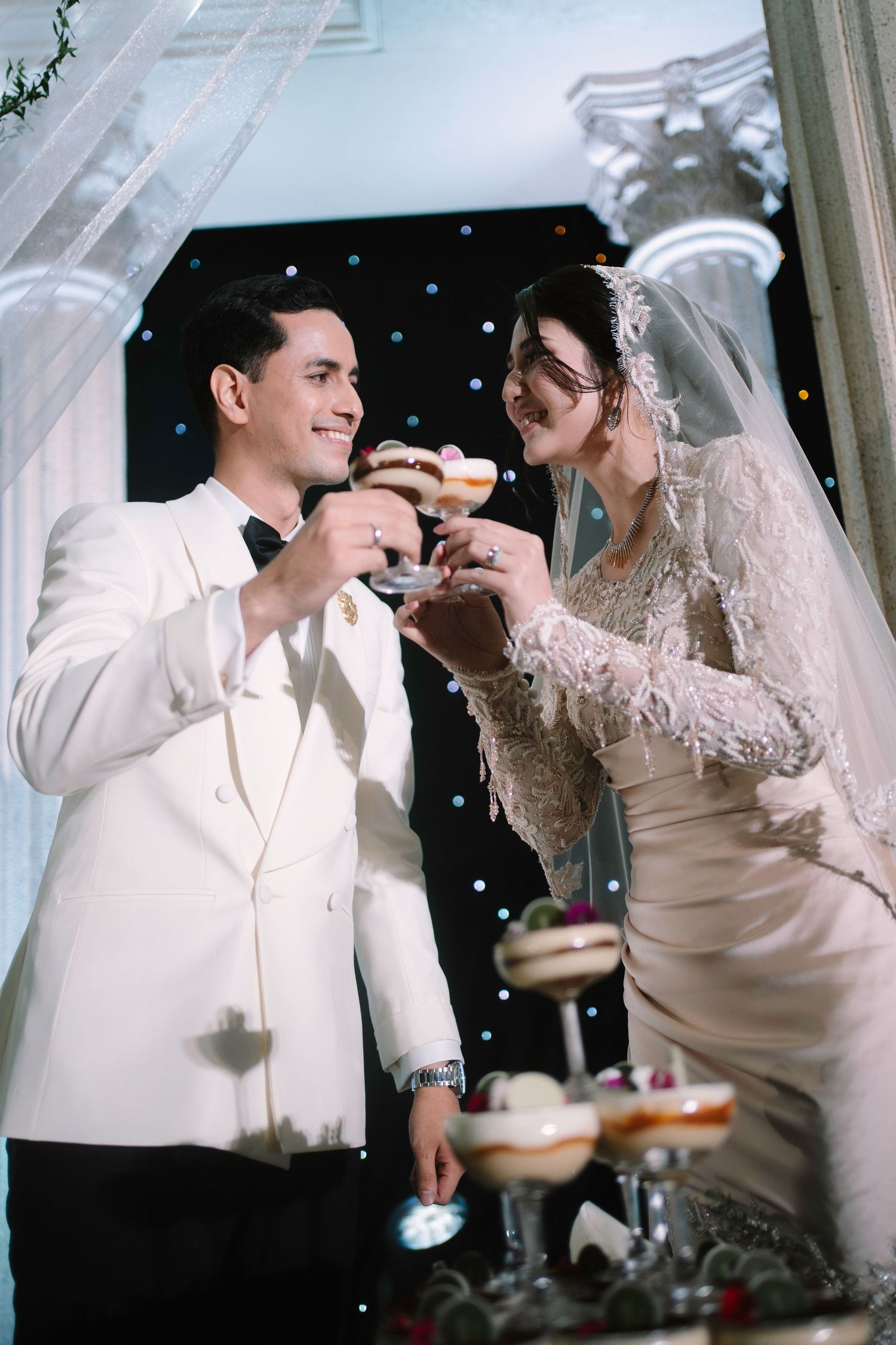 Bride and groom toasting with champagne glasses at elegant wedding reception in white attire.