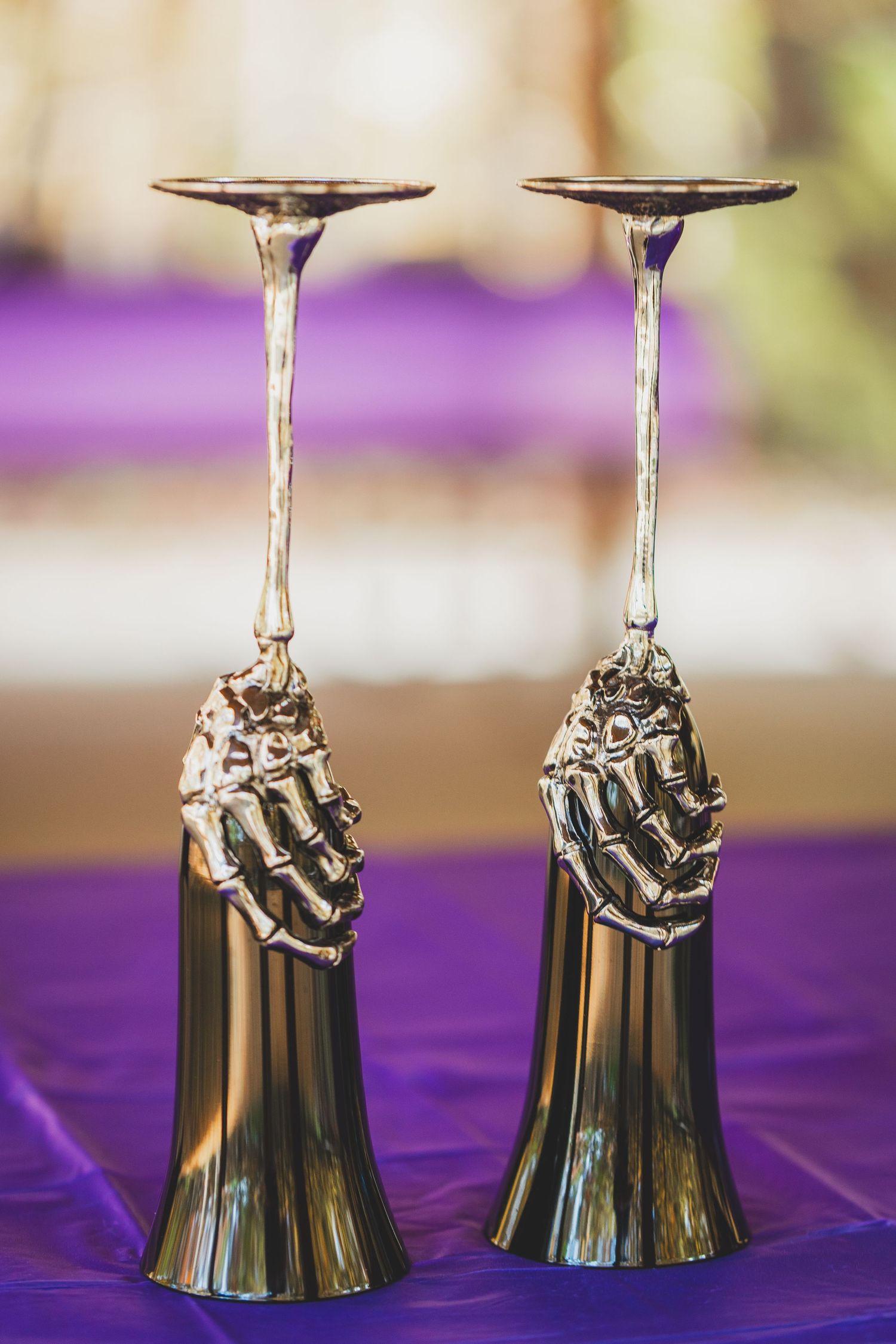 Two ornate silver candlestick holders with skeletal hand bases on a purple tablecloth.