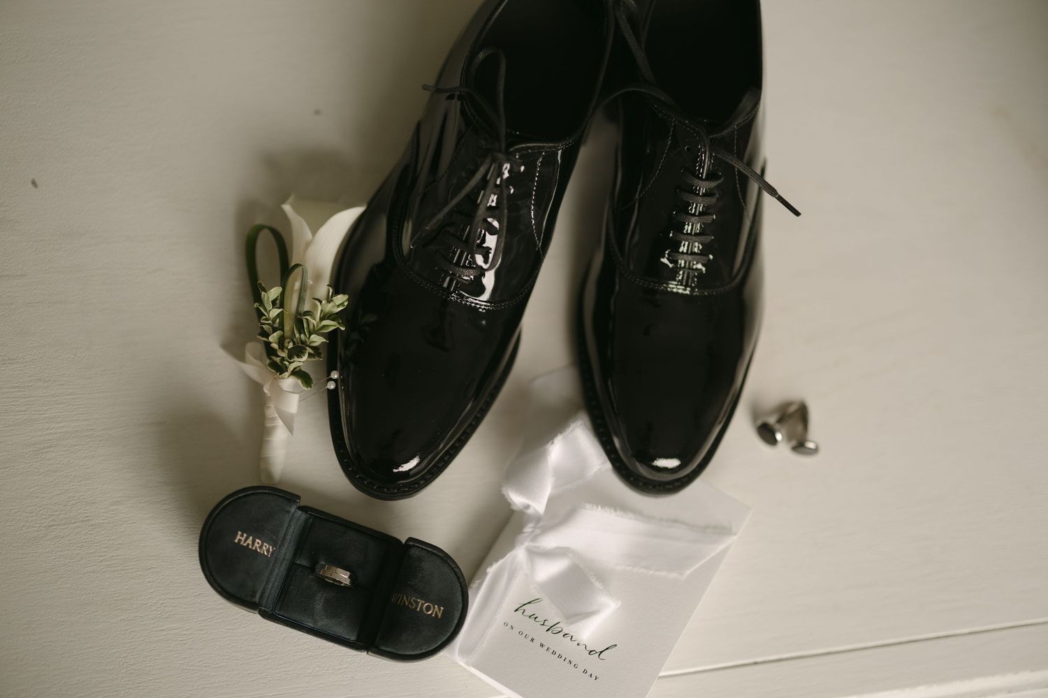 Groom wedding accessories flat lay with black patent leather dress shoes, boutonniere, and cufflinks.