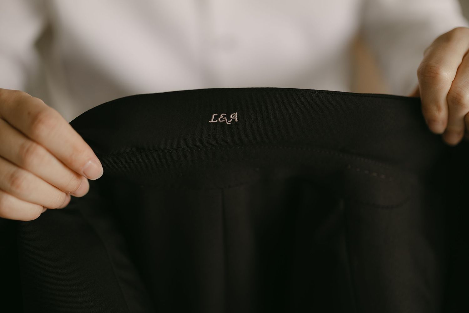 Close-up of black tuxedo jacket lining with embroidered initials LEA, held by groom before wedding.