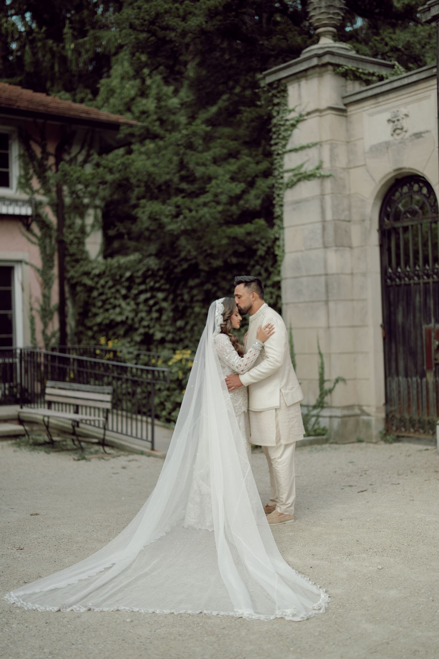 Couple in traditional South Asian wedding attire holding hands in a lush garden at sunset.