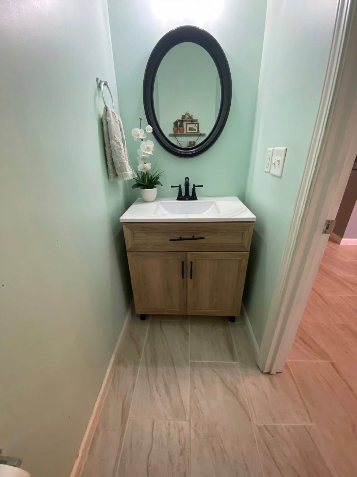Small bathroom with wood-look porcelain floor tiles and wooden vanity with oval mirror.