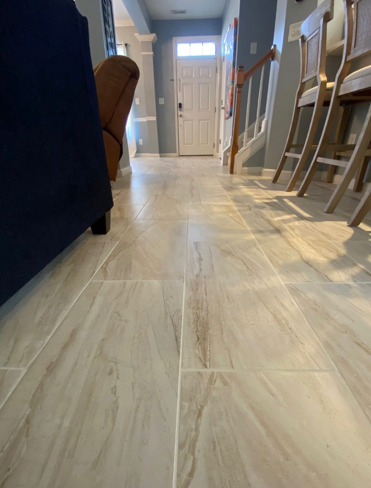Light beige marble-look porcelain tile flooring in a bright home entryway with staircase and blue sofa.