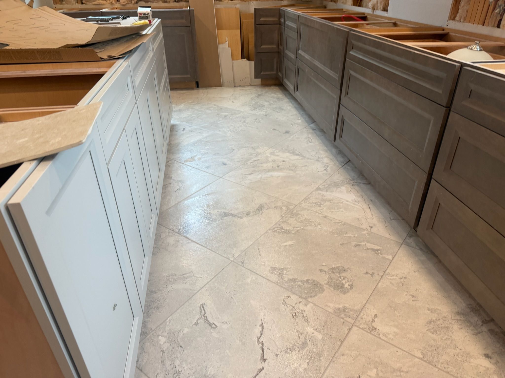 Gray kitchen cabinets installed over large format white marble porcelain tile in herringbone layout.