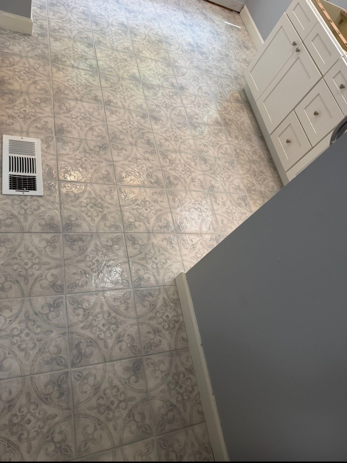Decorative gray and white patterned ceramic floor tiles installed in a bathroom near white vanity cabinetry.