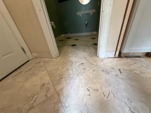 White marble porcelain floor tiles installed in hallway leading to green bathroom during renovation.