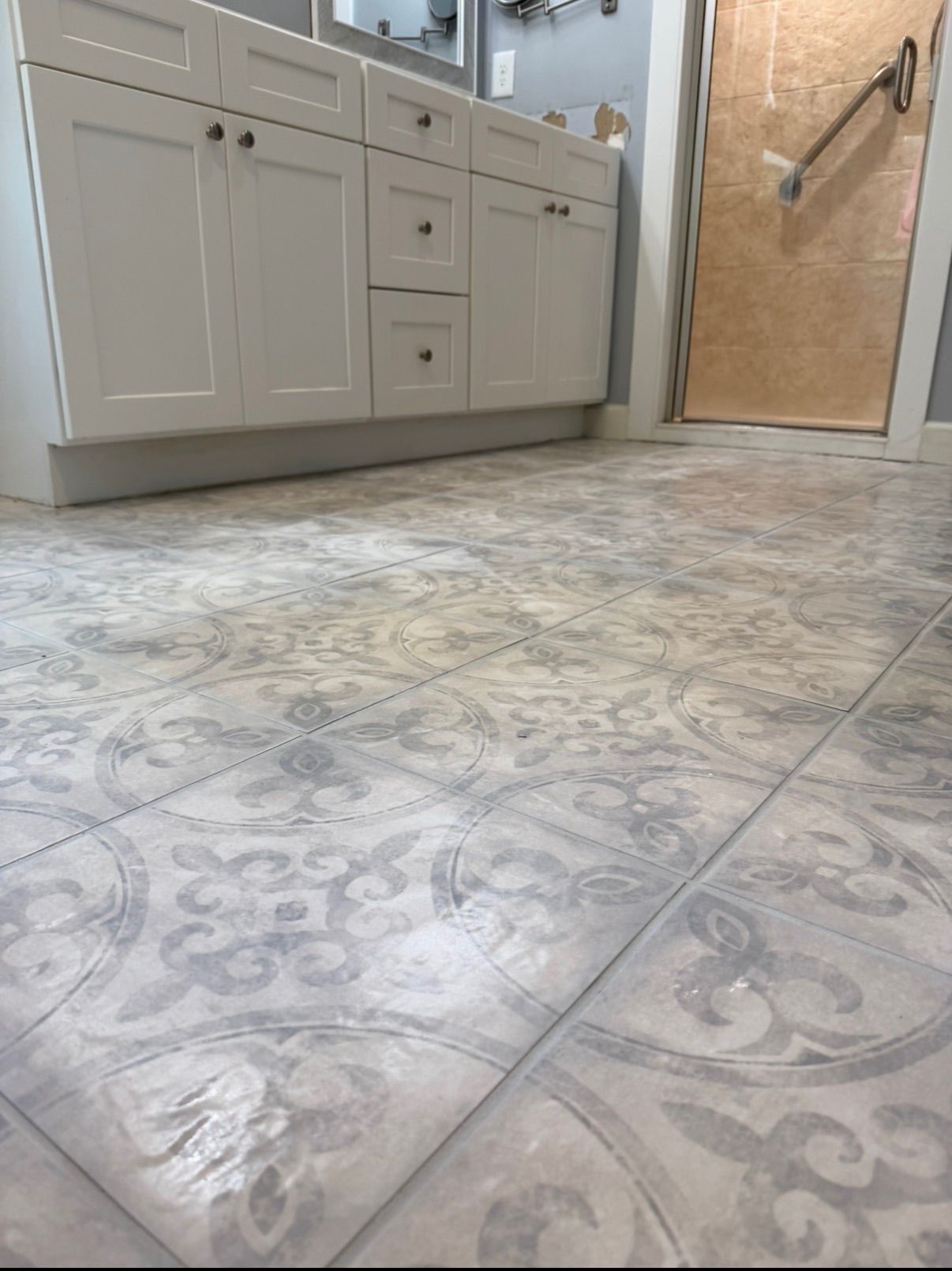 Bathroom floor with decorative gray patterned ceramic tiles in front of white vanity cabinet.