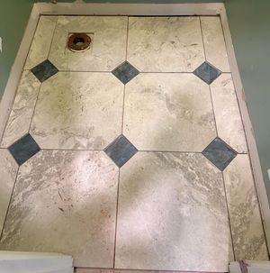 Beige marble shower floor tiles with decorative dark diamond accent tiles arranged in an elegant geometric pattern.
