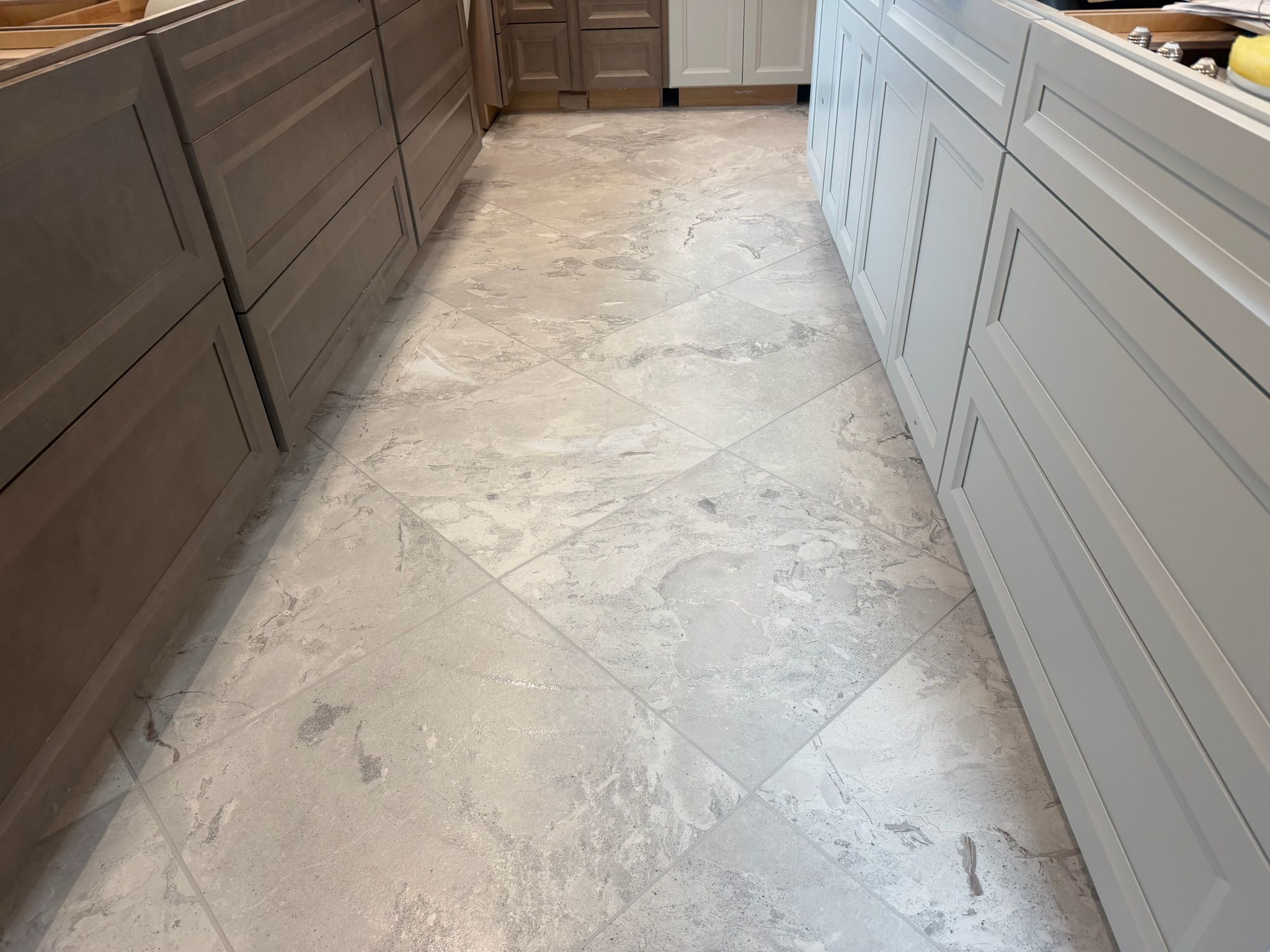 Large white marble tile flooring installed in diagonal pattern between dark wood and white kitchen cabinets.