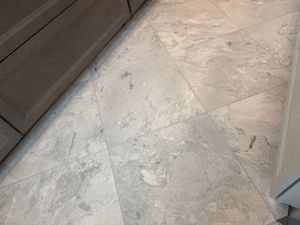 Close-up of white marble floor tiles with gray veining laid in diagonal pattern near kitchen cabinetry.