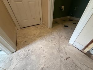 Large gray marble-look porcelain tiles installed diagonally in a hallway near white interior doors during renovation.