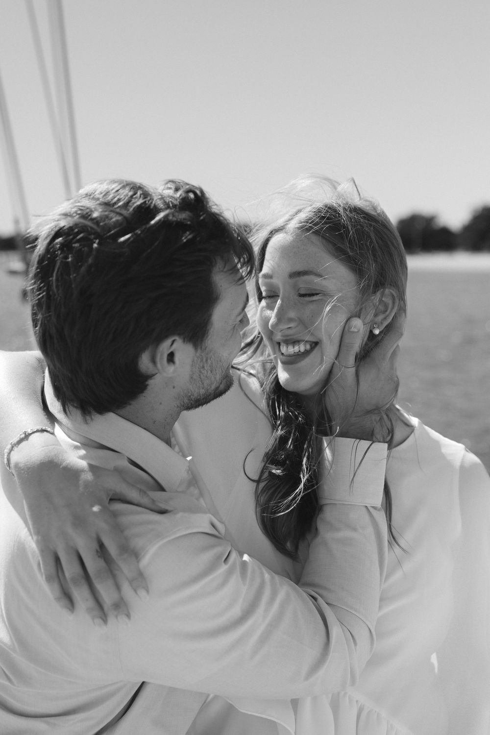 Black and white photo of a happy couple embracing and smiling on a sailboat, the man gently holding the womans face.