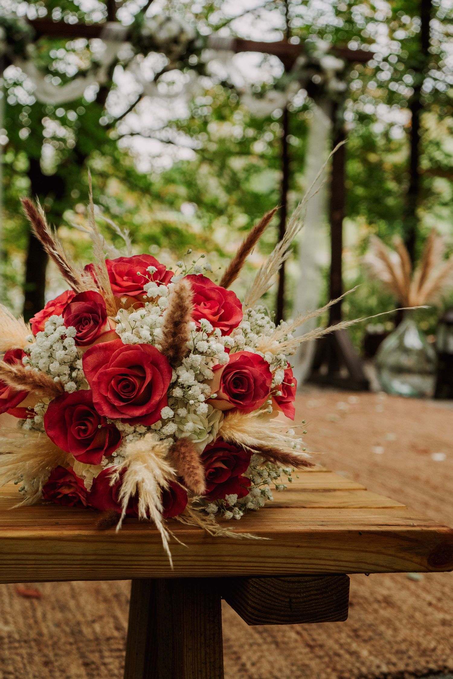 Bouquet of pink roses with babies breath laying on a bench with forest ceremony area in the background. Dayton, Ohio.