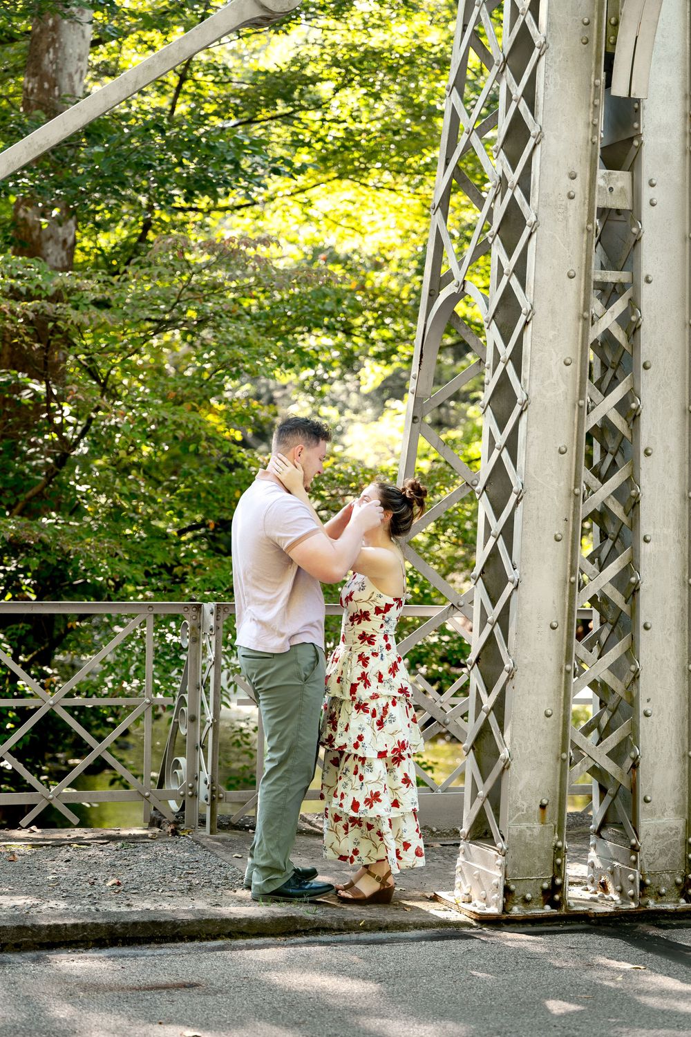 Couple sharing a romantic moment on a vintage iron bridge surrounded by lush green trees.