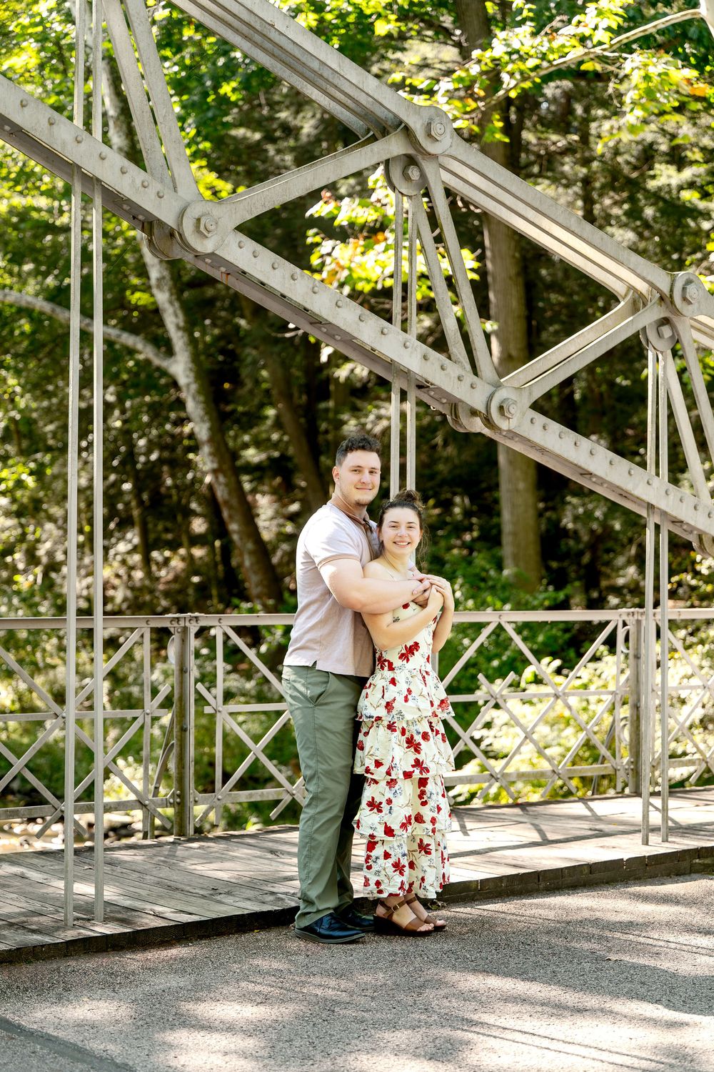 Happy couple embracing on a vintage metal bridge surrounded by lush green forest trees.