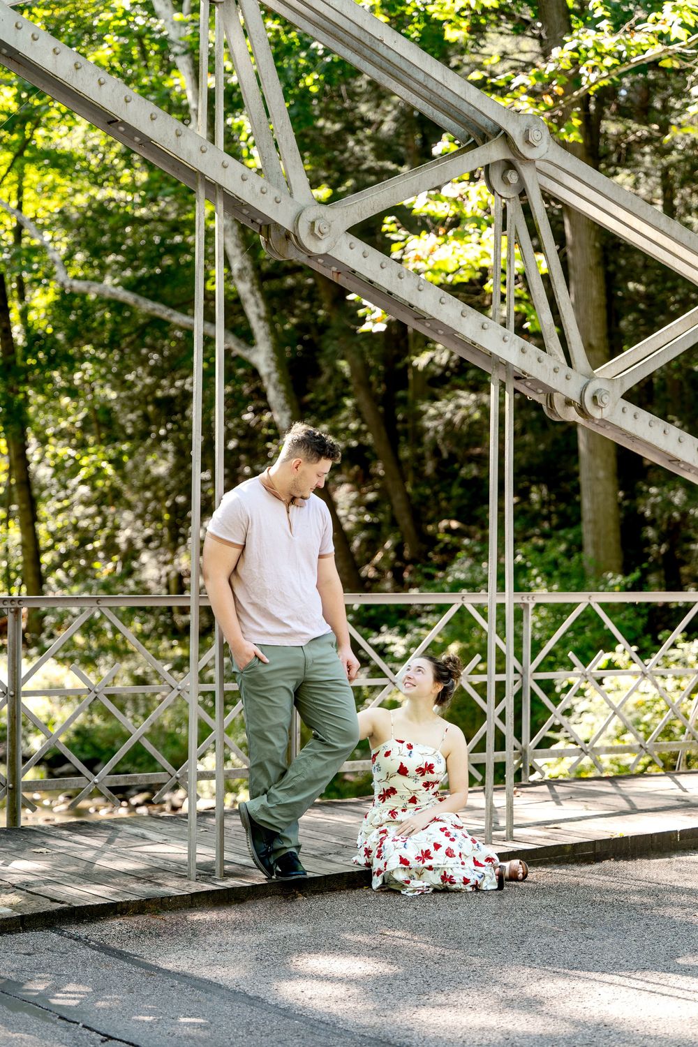 Young couple sharing a playful moment on a white iron bridge with green trees in background.