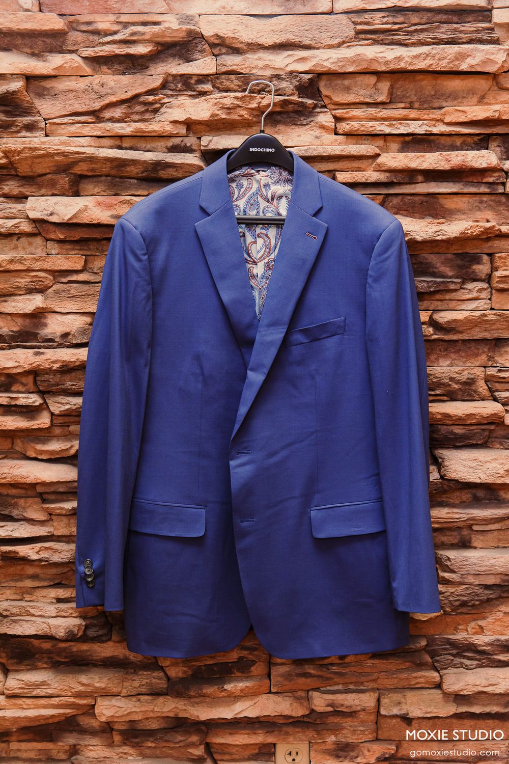Blue men's suit jacket hanging on a hanger against a rustic brick wall, perfect for a formal wedding.