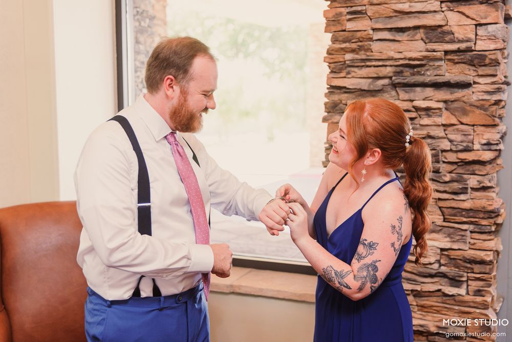 Groom in suspenders and bride with tattoos share a joyful handshake moment at their wedding venue.