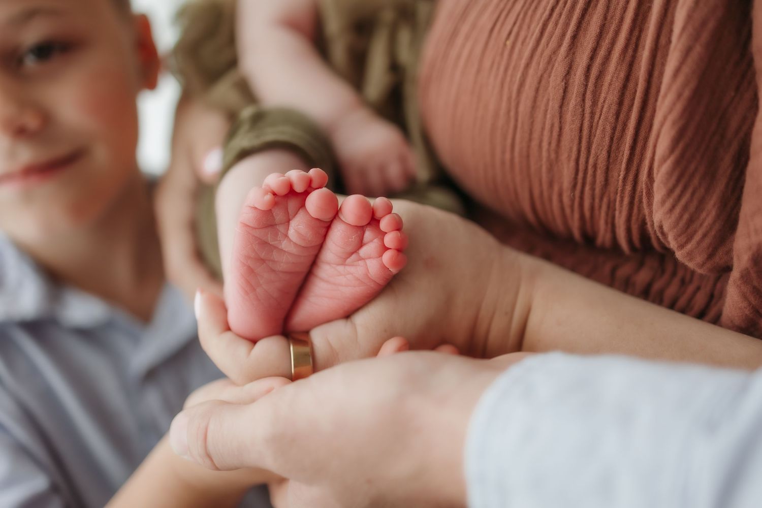 A parent and child gently cradle a newborn baby's tiny feet in their hands during a family newborn photography session.