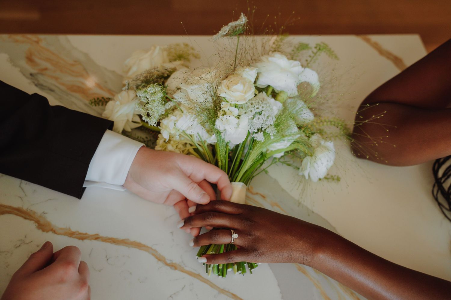 Wedding party celebrates bride and groom outdoors, raising flowers, with evergreen trees in background.