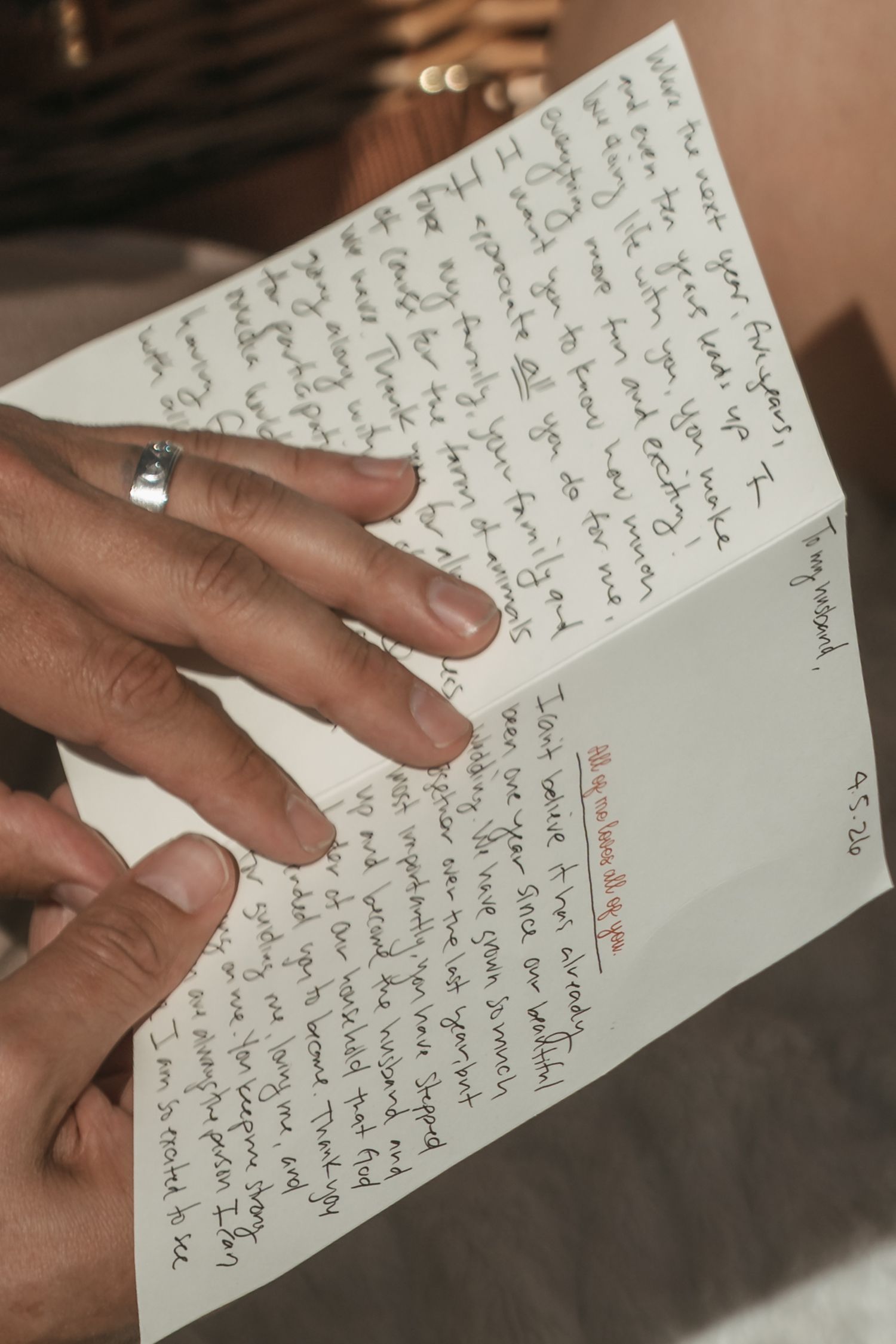 Hands holding a handwritten letter with cursive writing, person wearing a silver ring reading personal correspondence.