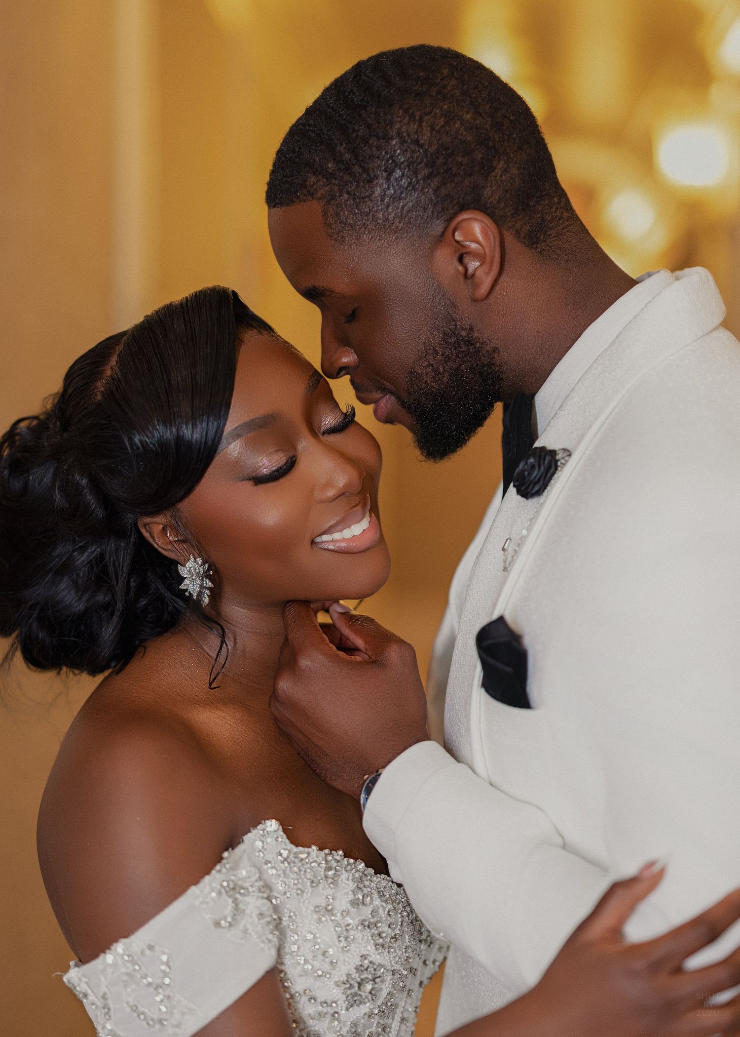 Elegant bride and groom share a romantic moment, dressed in white wedding attire with soft glowing background.
