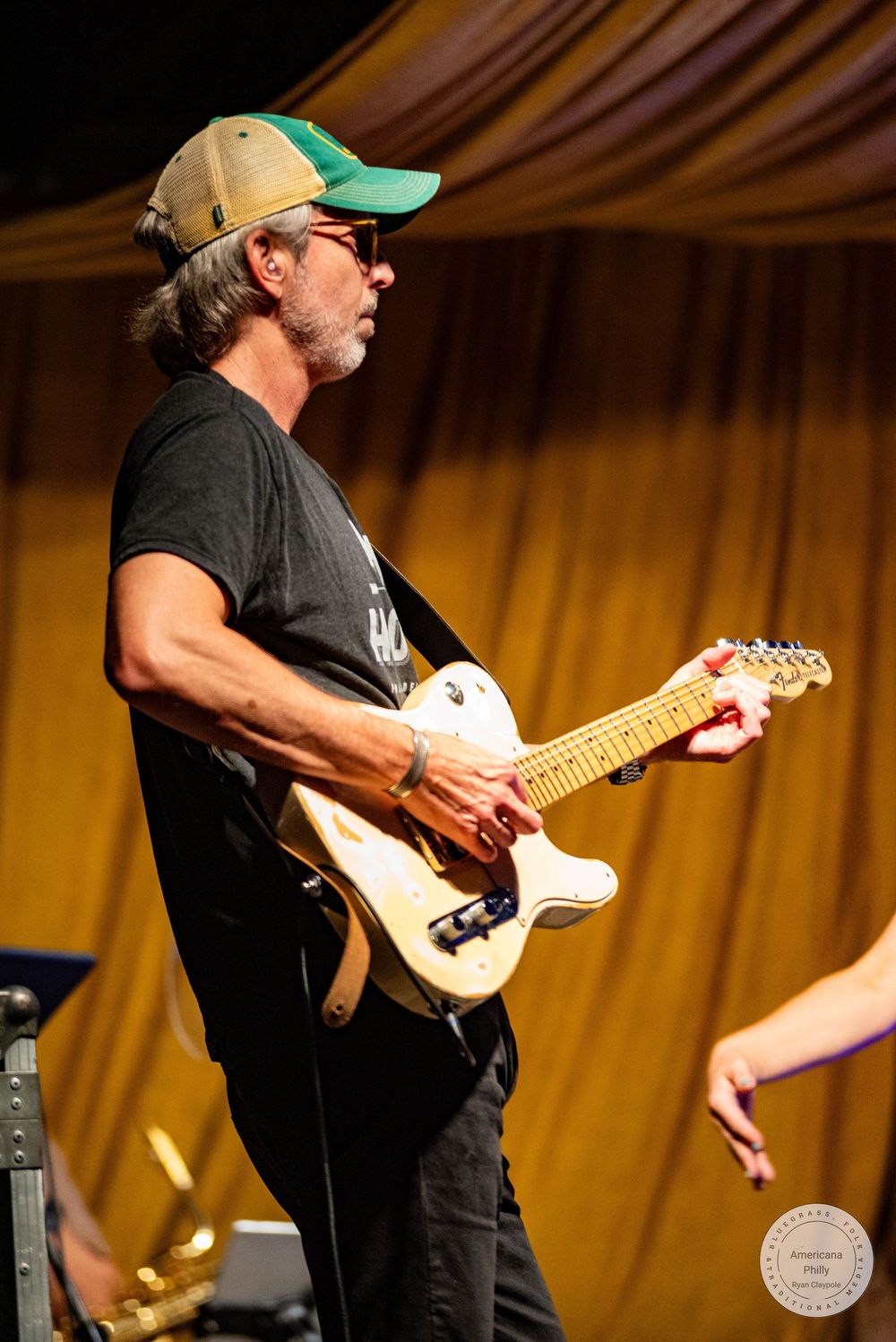 Man in green cap playing white electric guitar on stage at live music event.