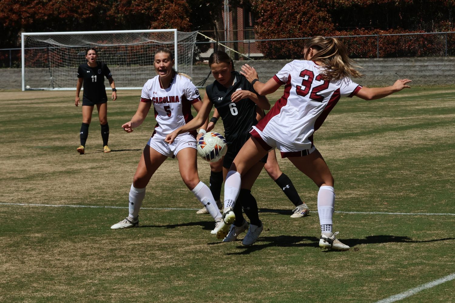 Three women's soccer players battle for possession of the ball.