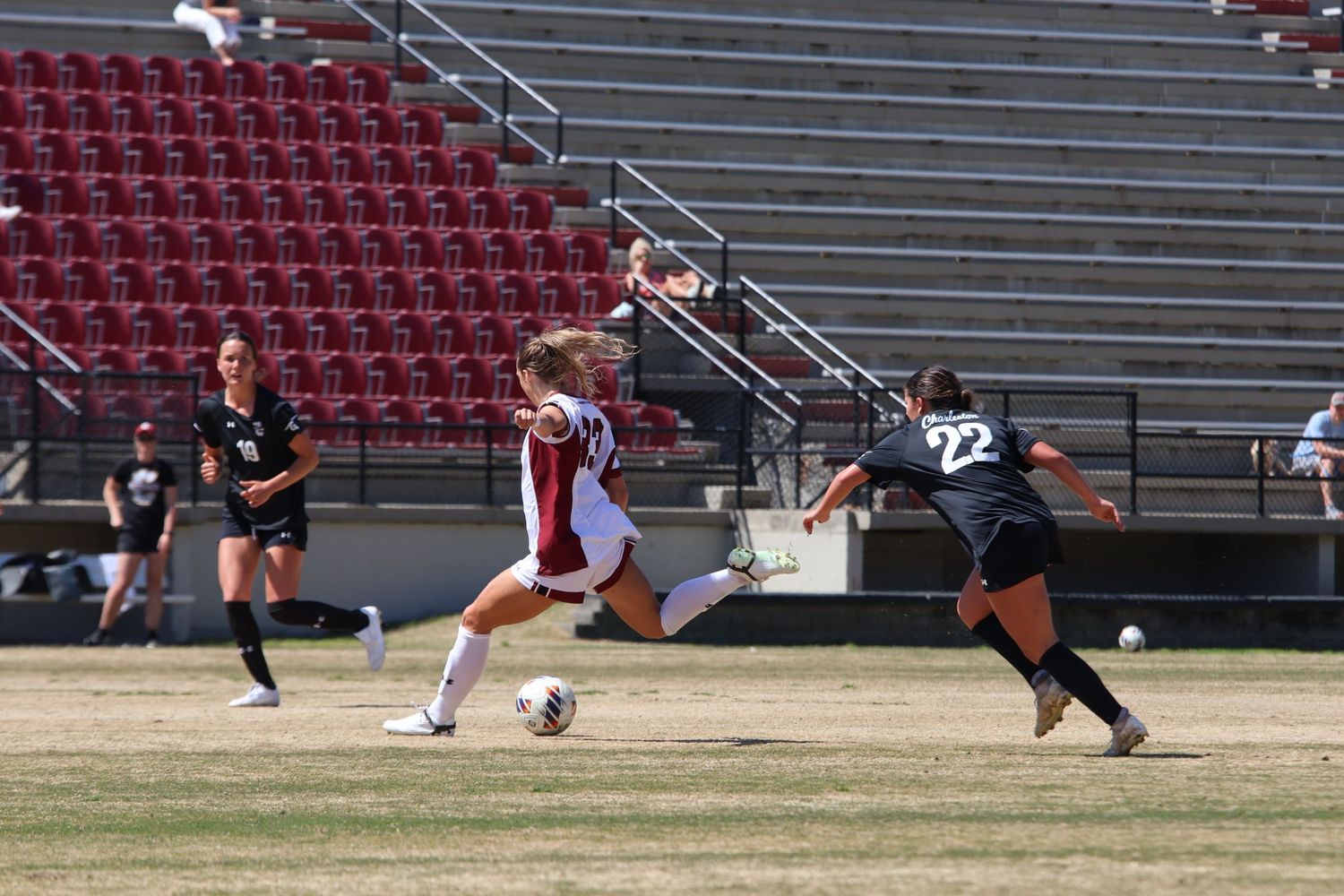 South Carolina women's soccer player kicks the ball as two defenders approach.