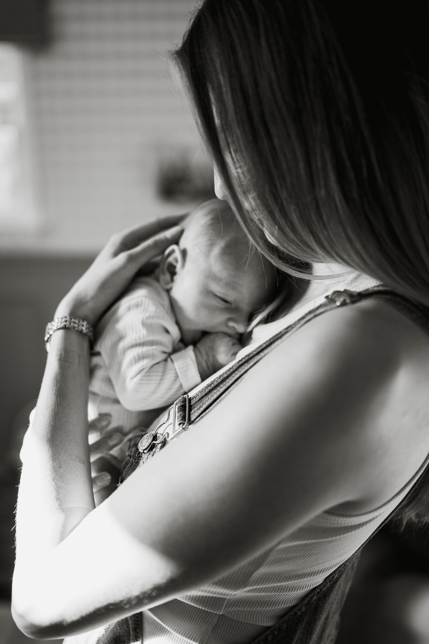 Black and white photo of a mother tenderly cradling her sleeping newborn baby close to her chest.