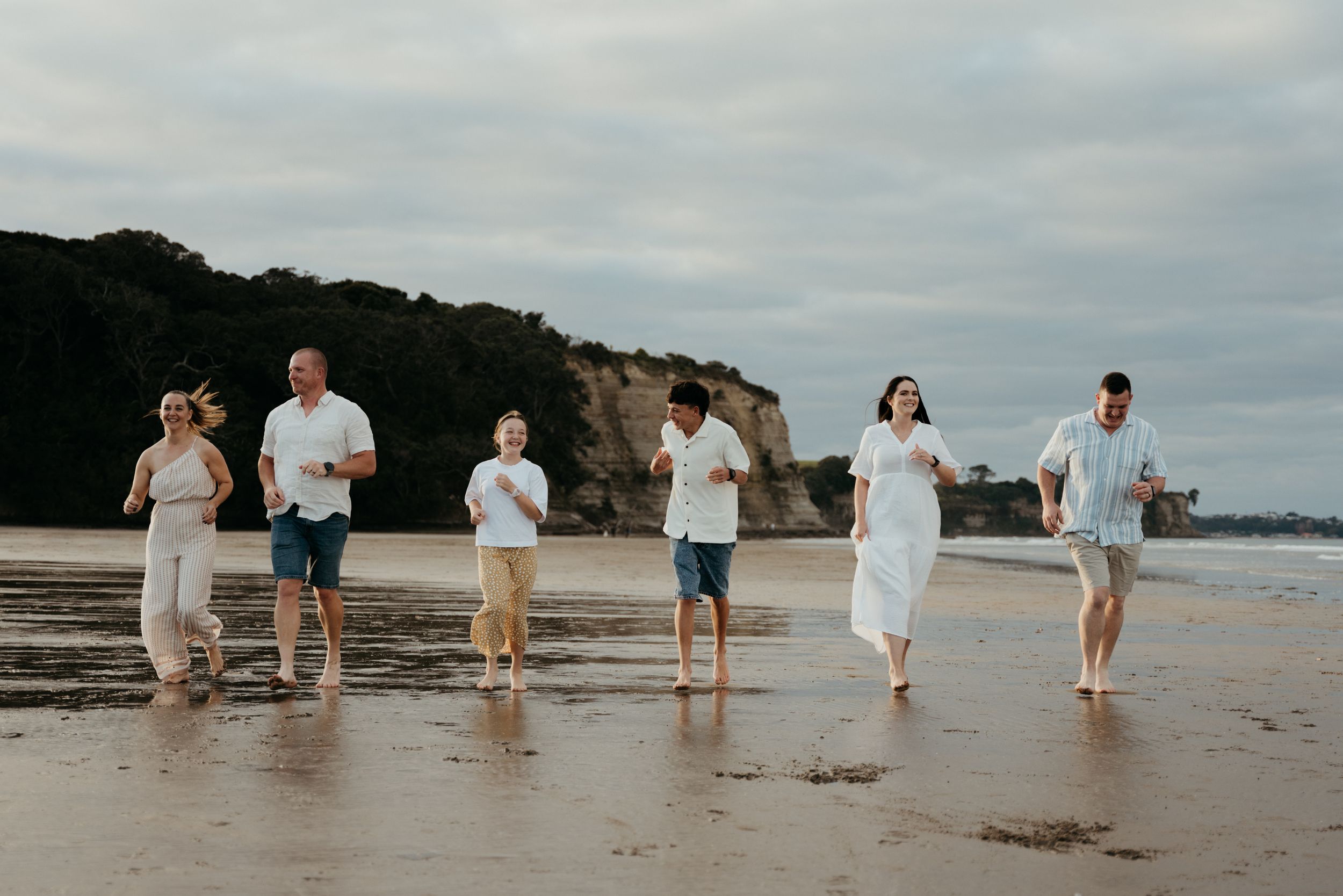 Family of six walking and running together on a sandy beach with rocky cliffs in the background.