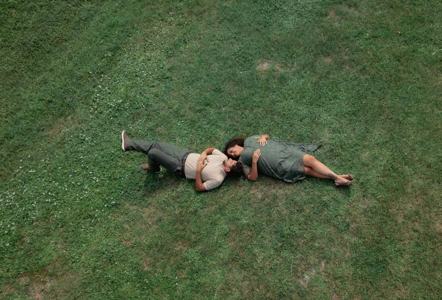 Aerial view of a couple lying together on lush green grass, relaxing outdoors on a sunny day.