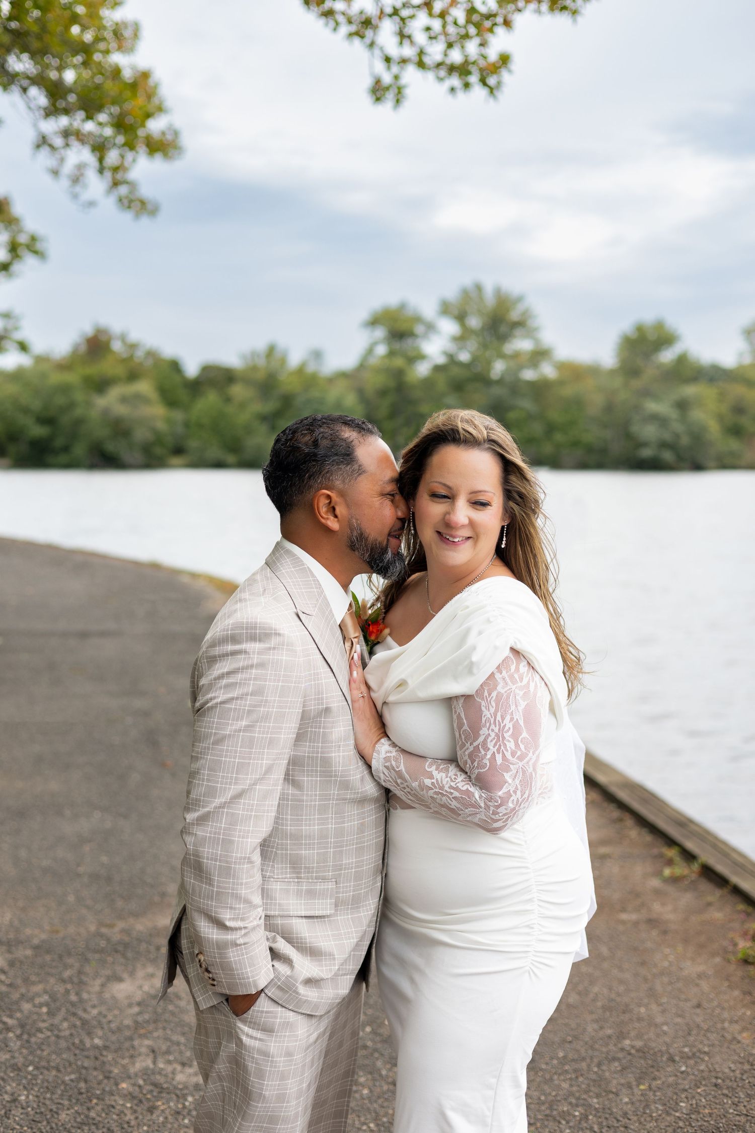 A couple embraces lovingly on a dirt path beside tall ornamental grasses on an overcast afternoon.