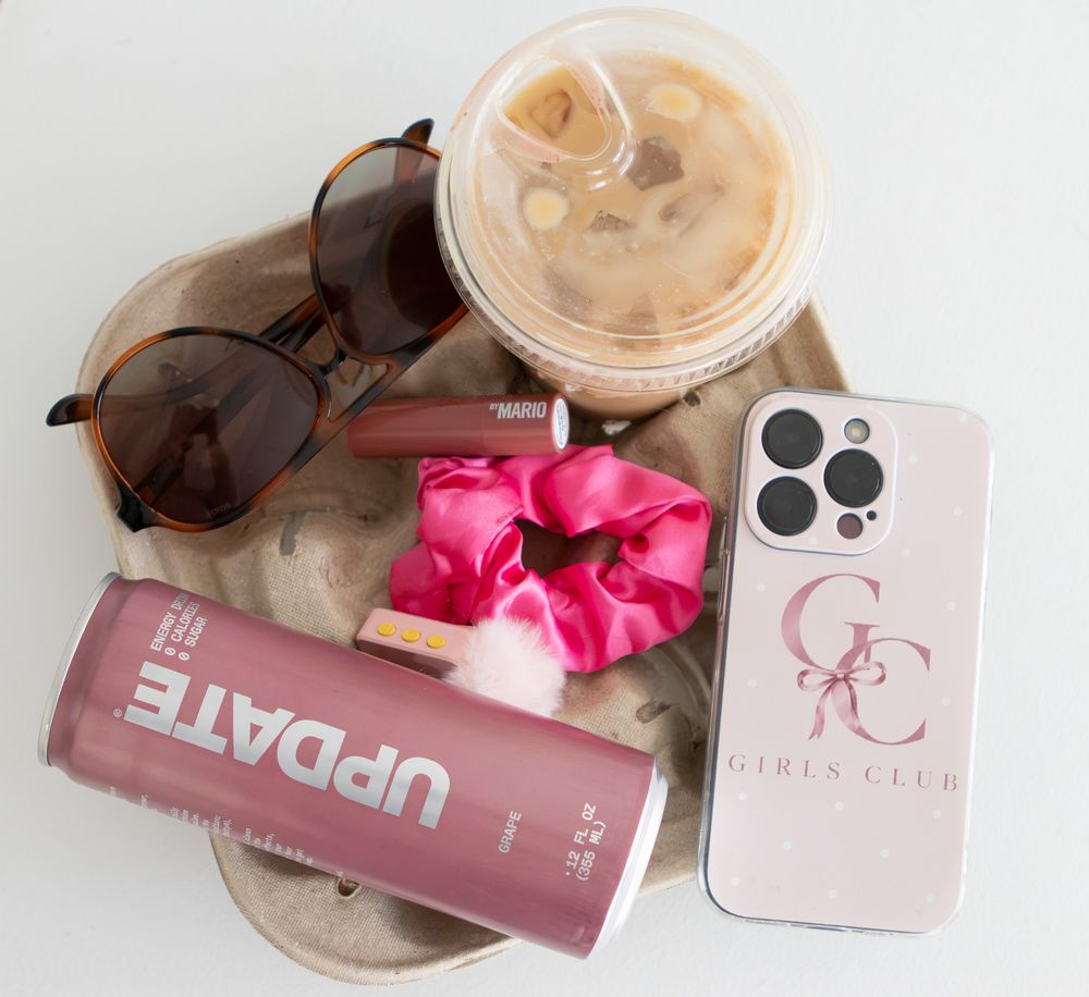 Flat lay of iced coffee, sunglasses, pink scrunchie, UPDATE energy drink, and Girls Club phone case.
