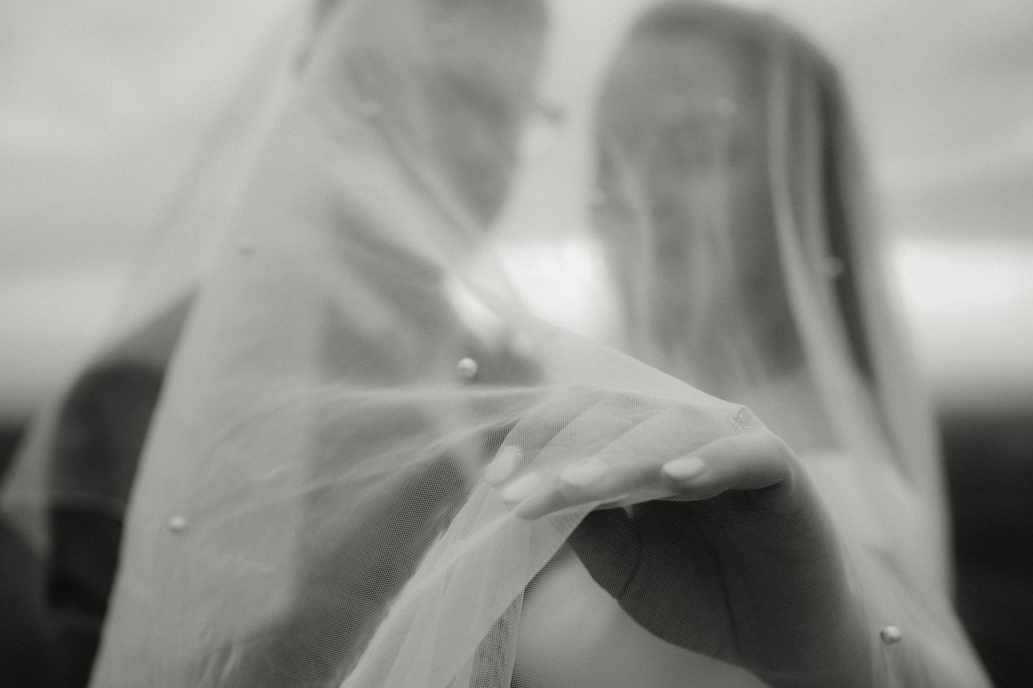Dreamy black and white photo of couple embracing under pearl veil.