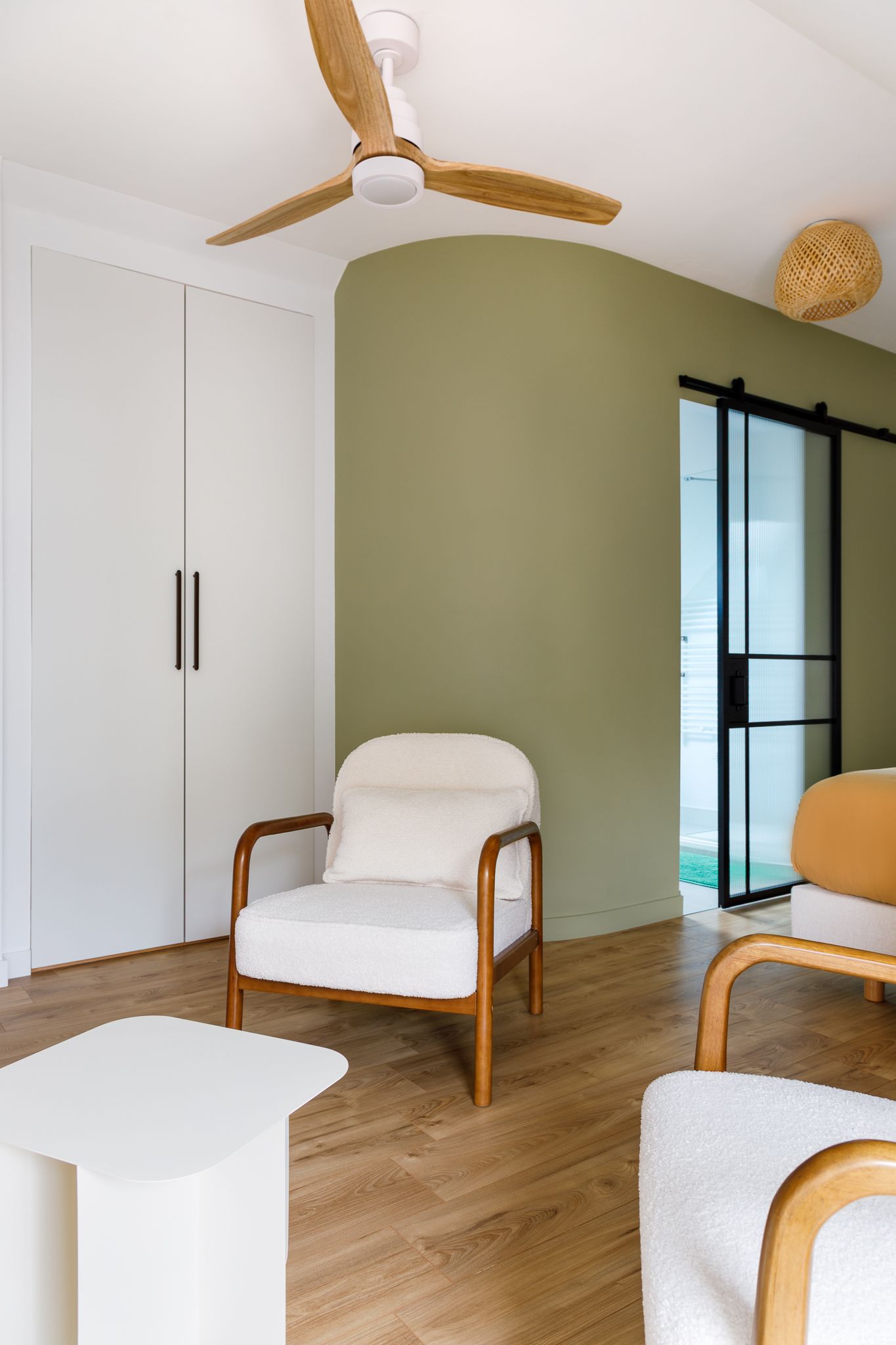 Chambre contemporaine avec un mur d'accent incurvé vert olive, un fauteuil en tissu bouclé blanc, un ventilateur de plafond en bois