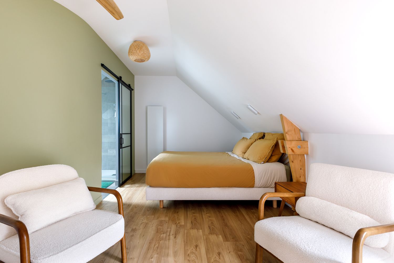 Aménagement d'une chambre mansardée lumineuse aux murs vert sauge et couvre-lit moutarde, photographie d'intérieur.