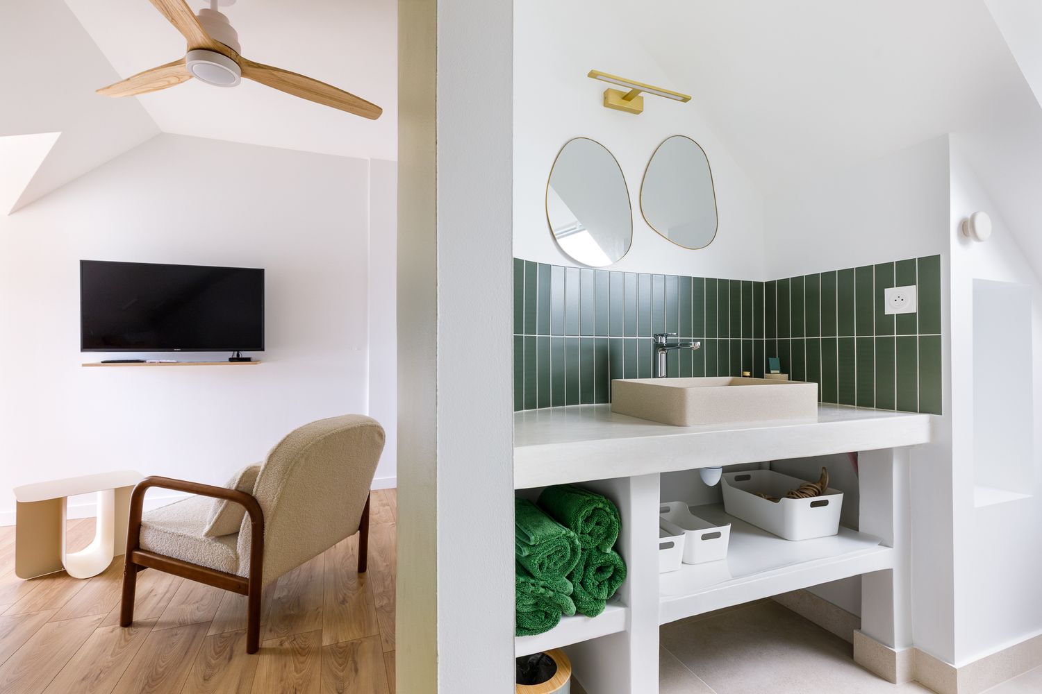 Chambre moderne équipée d'un ventilateur de plafond, d'une télévision murale, d'un fauteuil et d'une salle de bains attenante