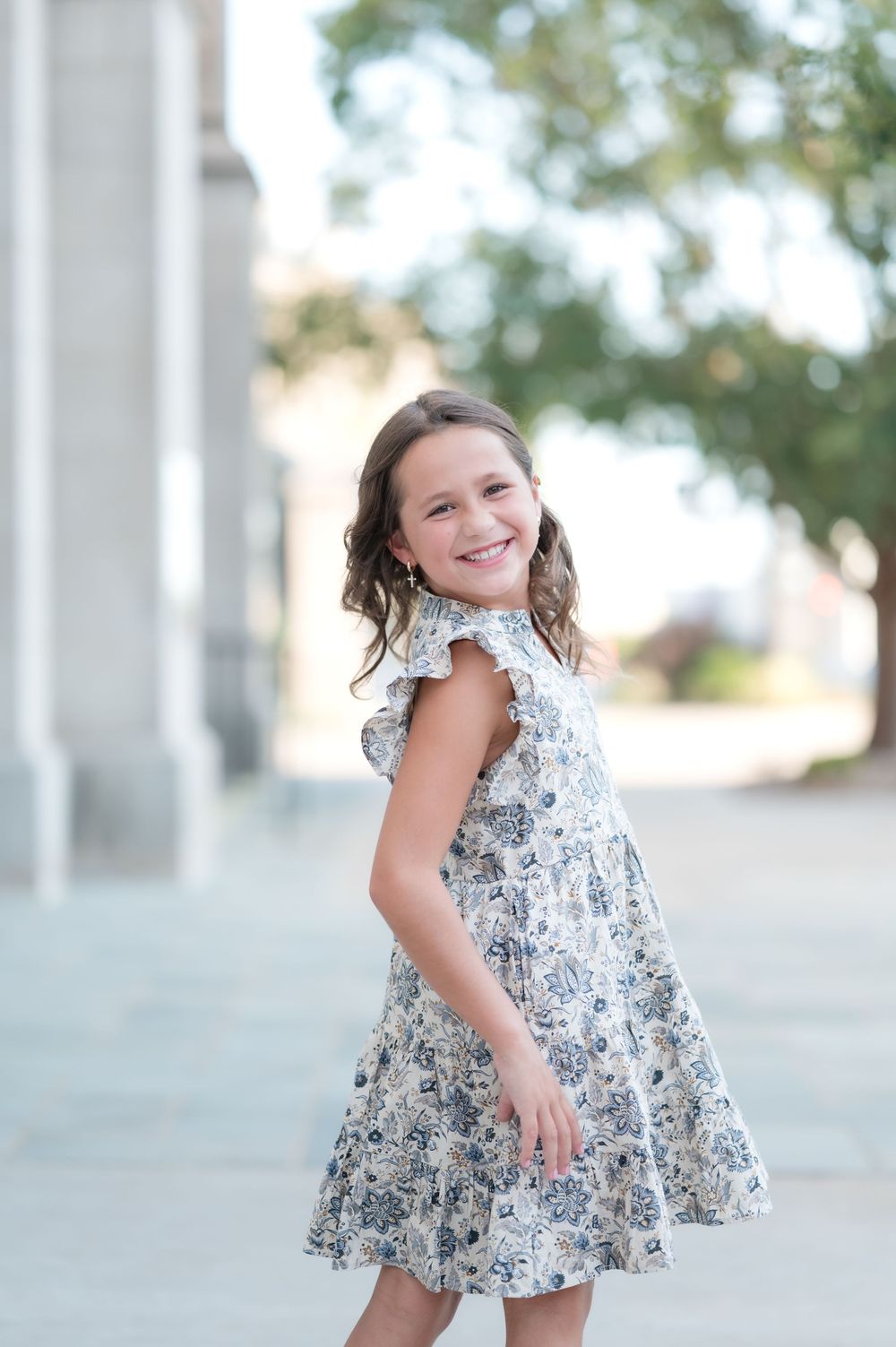 Young girl in floral dress smiling outdoors near stone columns.