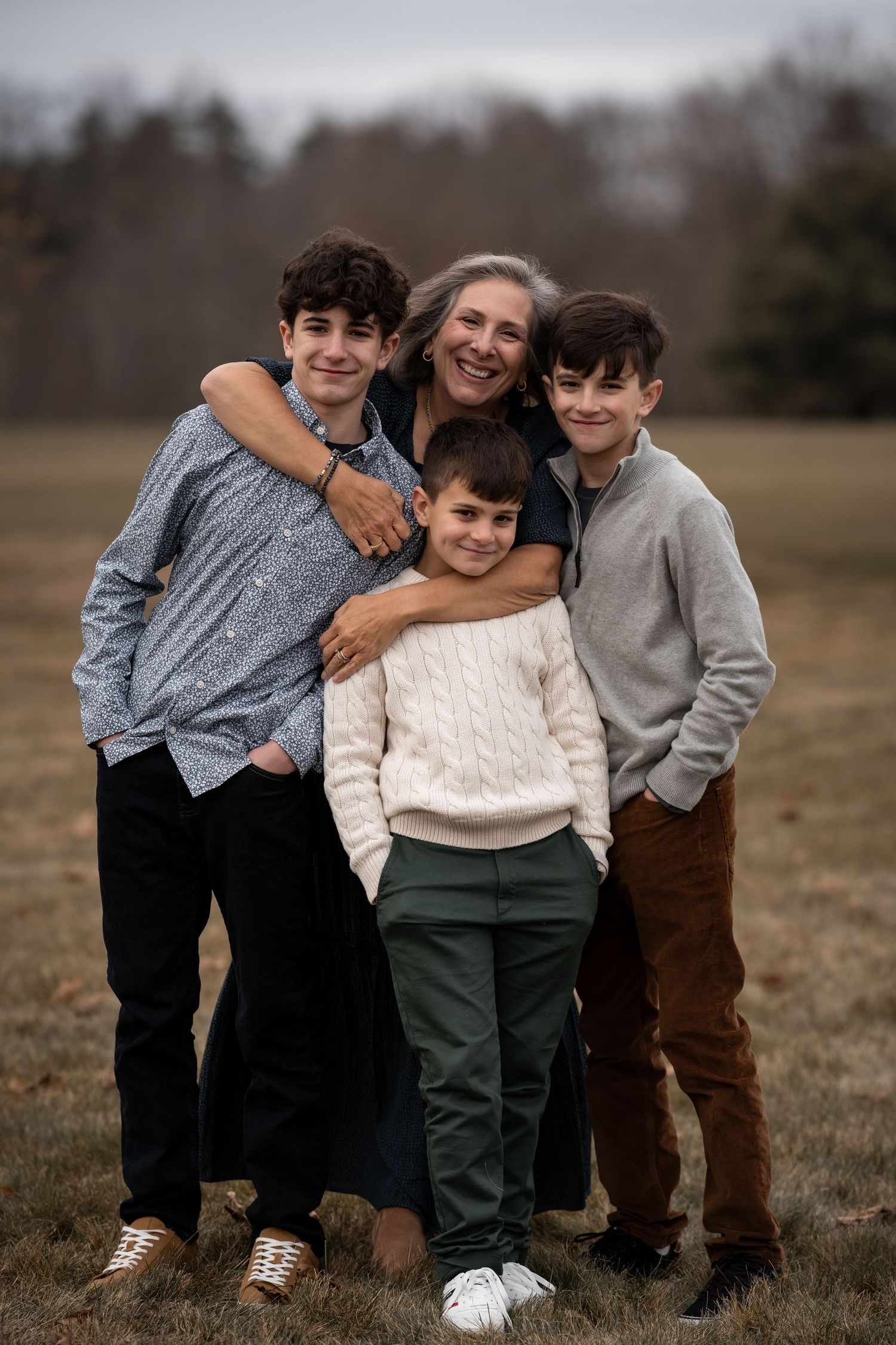 A family of four wearing cozy sweaters poses together outdoors in a field on an overcast day.