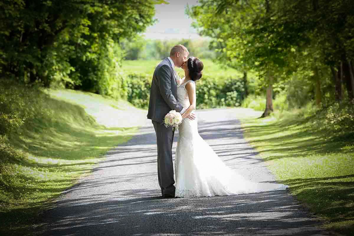 Bride and groom sharing a romantic kiss on a tree-lined path at Hundith Hill wedding venue Cockermoith