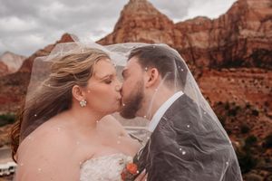 Bride and groom kissing under a flowing veil with red rock canyon formations in the background.